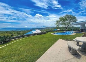 Un patio trasero con piscina, una mesa de patio y vista al océano.
