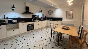 A modern kitchen with a black countertop, white cabinets, a black oven, and a dining area with a wooden table and chairs.