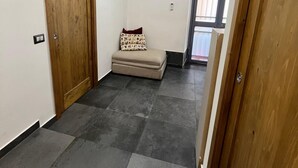 Een kamer met een houten deur, een kleine bank met een gestreept kussen, en een betegelde vloer.