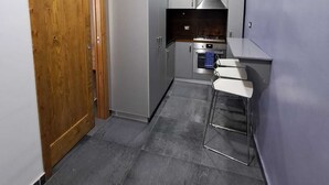 Een smalle gang met een houten deur, een keuken met een fornuis, en een eethoek met stoelen.