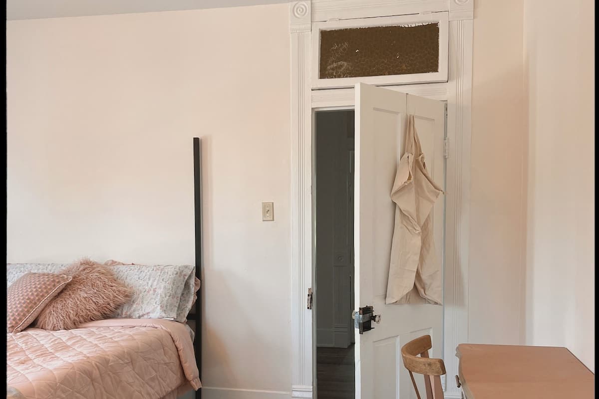 Quarto com cama, cadeira, mesa e porta que dá para outro espaço.
