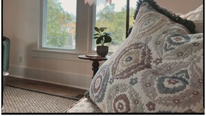 Et hyggeligt værelse med en mønstret pude, et lille bord med en plante og en hængende lampe.