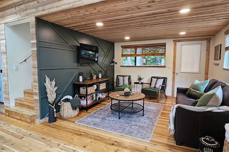 A cozy living room with a wooden floor, a round coffee table, a sofa, and a TV mounted on the wall.