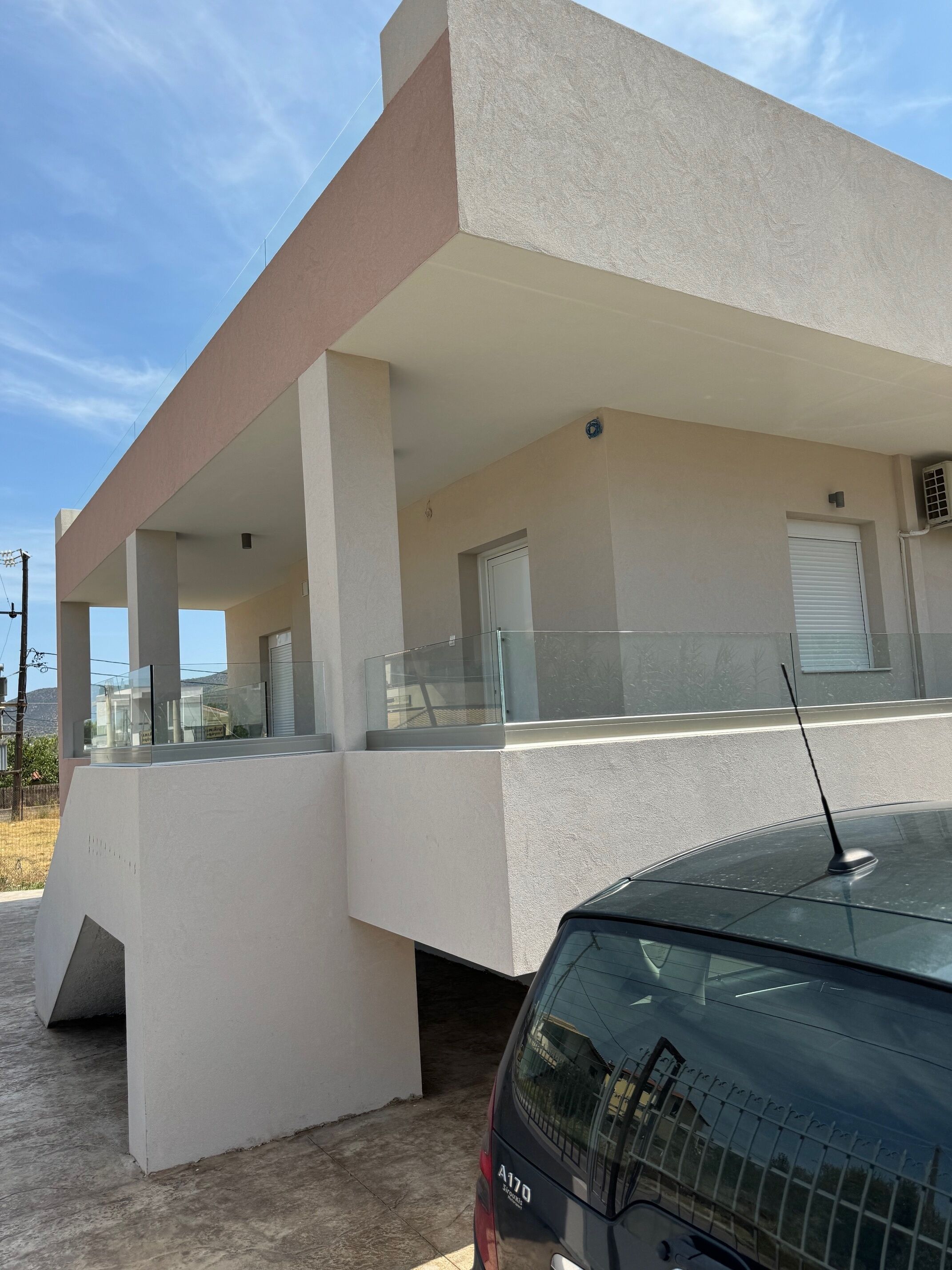 A modern building with a flat roof, large windows, and a covered outdoor area with glass railings.