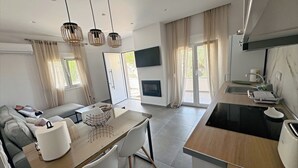 A modern kitchen with a built-in oven, a dining area with a glass table and chairs, and a living area with a sofa and a flat-screen TV.