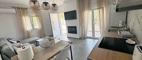 Uma cozinha moderna com forno embutido, um espaço de refeições com mesa e cadeiras de vidro, e uma sala de estar com sofá e TV de tela plana.