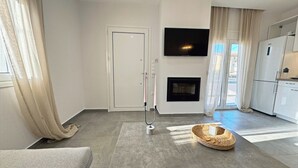 A modern living room with a sofa, a coffee table, a fireplace, and a kitchen area with a TV and refrigerator.