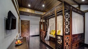A traditional room with a four-poster bed, a wooden table with fruit, and a TV mounted on the wall. - Xianting Inn (Liyang)