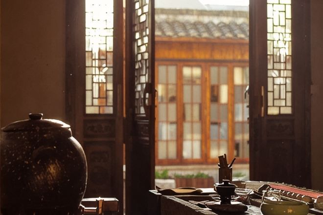 A traditional room with a large ceramic pot, a wooden table, and a view through a wooden door with glass panels.