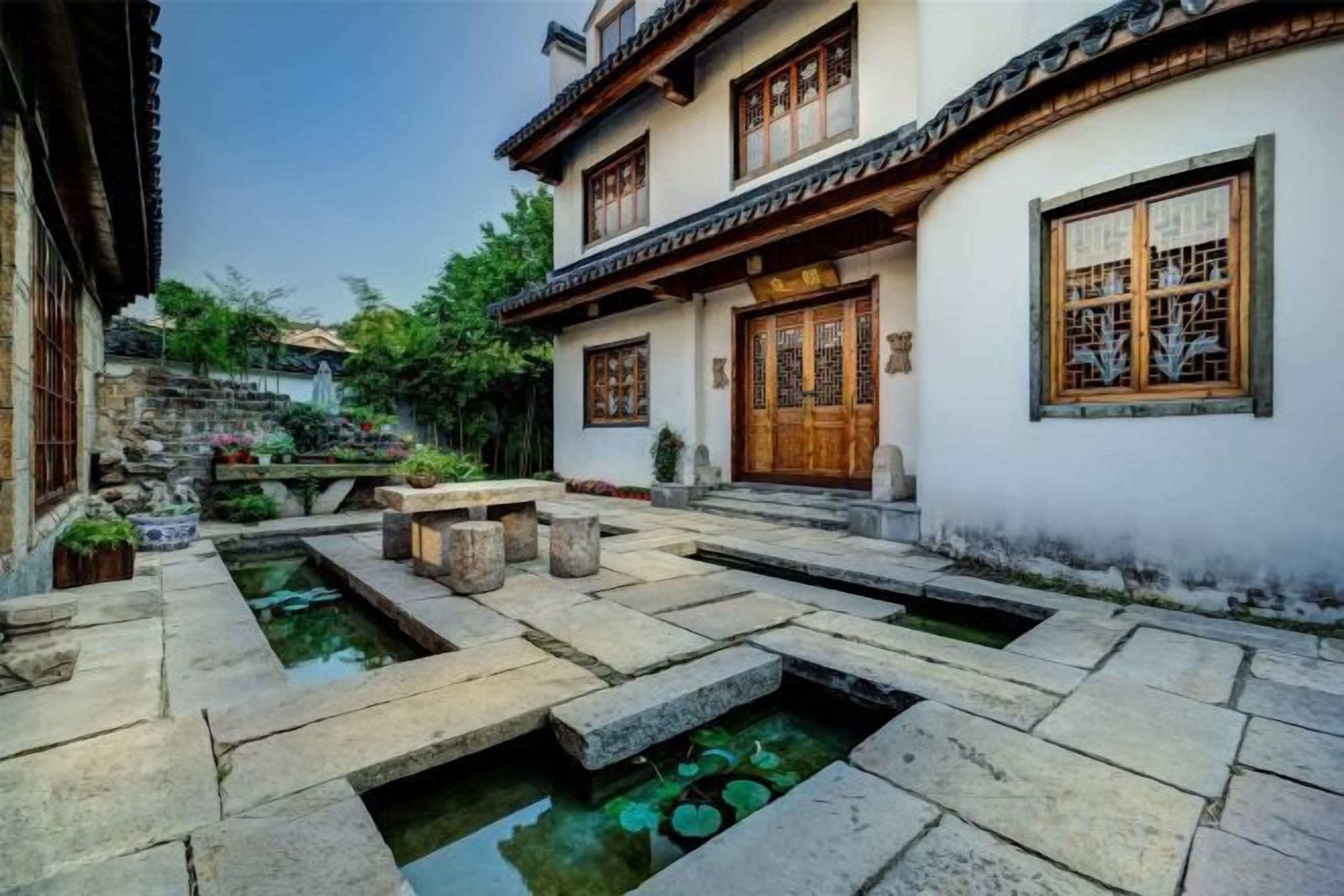 Un patio tradicional con senderos de piedra, una fuente pequeña y un edificio con puertas y ventanas de madera.
