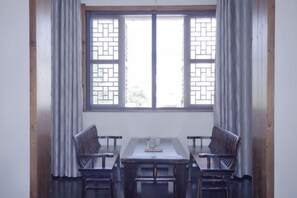 A room with a table and four chairs, a window with a traditional lattice design, and curtains. - Xianting Inn (Liyang)