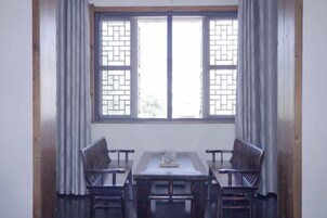 Una habitación con una mesa, cuatro sillas, un ventanal con un diseño de celosía tradicional y cortinas.