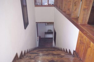 Una escalera de madera con barandilla, que lleva a una zona de descanso con una mesita y una silla.