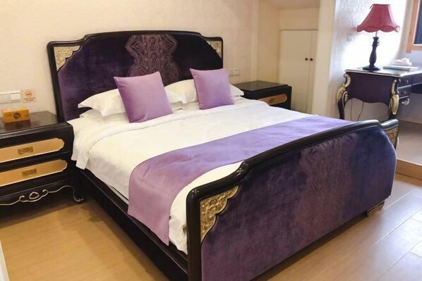 A bed with a purple headboard and white bedding, a nightstand with a lamp, and a wooden floor. - Xianting Inn (Liyang)
