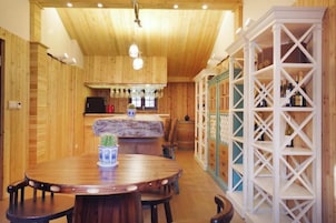 Un interior de madera con una mesa redonda para comer, sillas, una zona de cocina y un estante blanco.