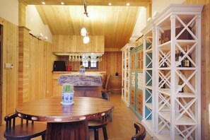 Un interior de madera con una mesa redonda para comer, sillas, una zona de cocina y un estante blanco.