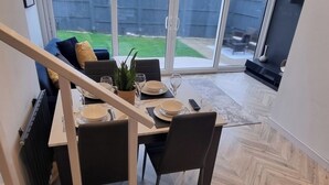 Zona pranzo con tavolo apparecchiato per quattro, una scala che conduce a un livello superiore e vista sul giardino retrostante attraverso ampie vetrate.