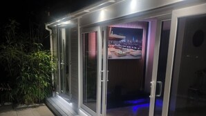 Una casa moderna con ampie vetrate che si aprono su un interno luminoso, una zona patio con tavolo e sedie, e vista sulla città illuminata di notte.
