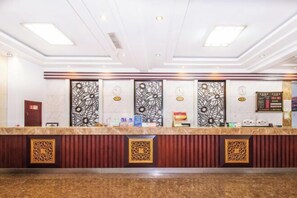 Een hotel receptie met een marmeren balie, decoratieve panelen, klokken en een informatiebord.