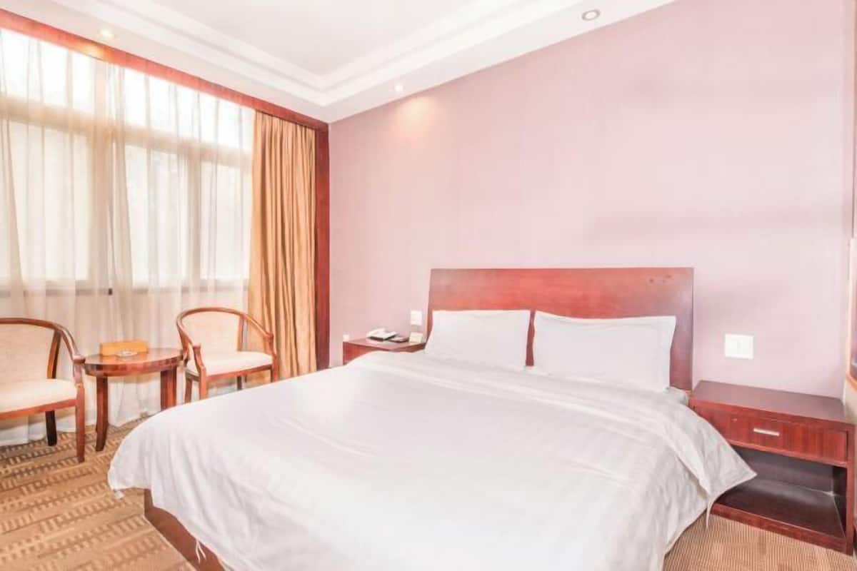 A hotel room with a large bed, two chairs, a small table, and a nightstand.