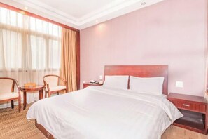 Een hotelkamer met een groot bed, twee stoelen, een klein tafeltje en een nachtkastje.