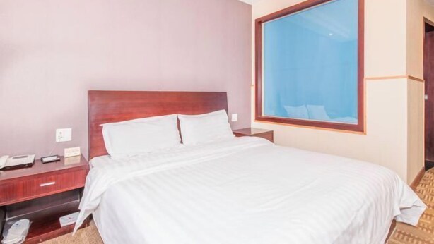 A hotel room with a large bed, a wooden headboard, a nightstand, and a window with a view. - Yindu Hotel (Pinghu)