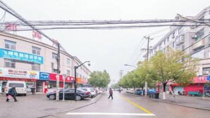 A street with buildings, parked cars, and overhead power lines. - Yindu Hotel (Pinghu)