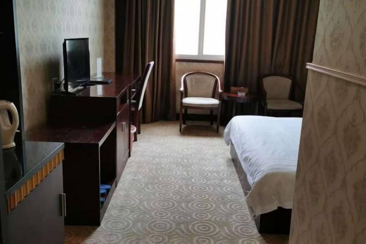 A hotel room with a bed, a desk with a computer, two chairs, and a window with curtains.