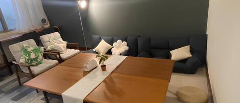Una sala moderna con una mesa de comedor de madera, un sofá con almohadones decorativos, una planta en maceta y una lámpara de pie.