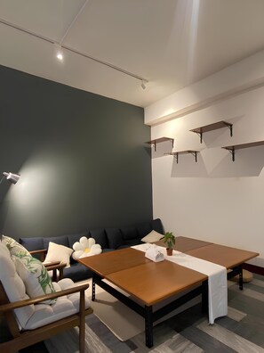 A modern room with a dark green accent wall, a wooden table, a sofa with cushions, and a small potted plant.
