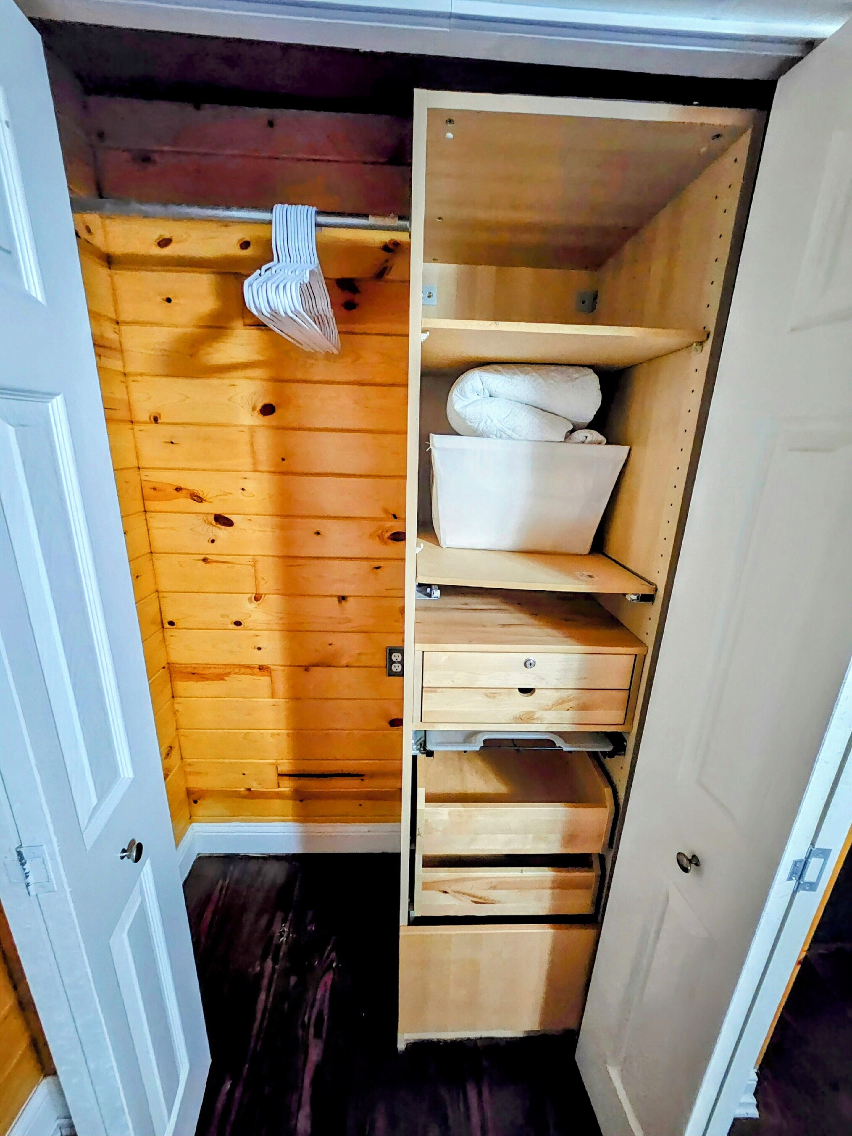 Un armario de madera con varios estantes y cajones, una barra para colgar ropa y una puerta blanca.