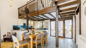 Un vaste espace dédié à la salle à manger, avec une table et des chaises en bois, une cuisine à l’arrière-plan et un balcon doté d’une balustrade en bois.
