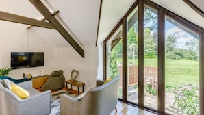 Un salon moderne doté d’une grande fenêtre, de poutres en bois, d’un téléviseur à écran plat et de sièges confortables.