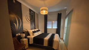 A modern bedroom with a large bed, a bedside table, a chair, and a wall with abstract art. - 3beds Villa w/ Pool - Near Almeria Beaches (Cantoria)