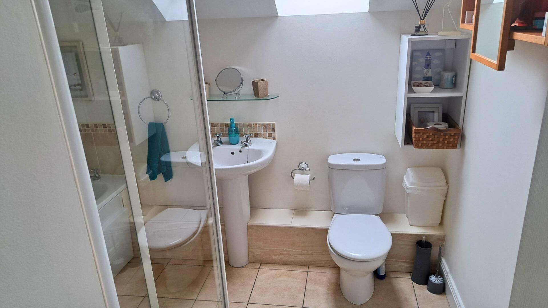 Un baño pequeño con cabina de ducha de vidrio, un lavamanos blanco, un inodoro y una pequeña repisa con artículos de aseo.