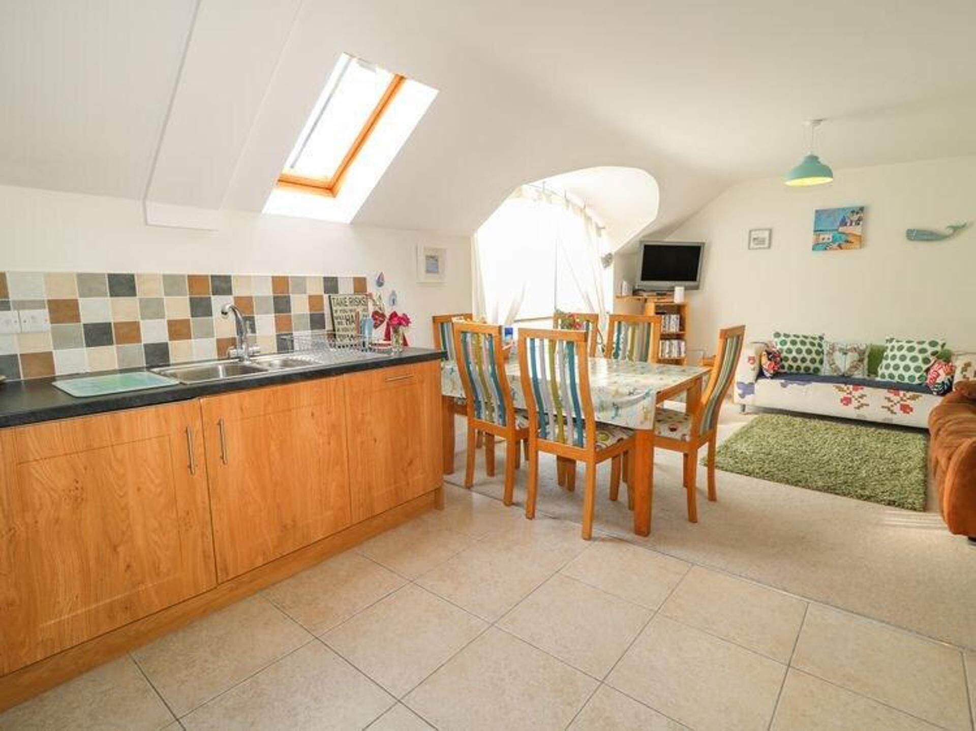 A compact kitchen with a dining area, a TV, and a sofa.