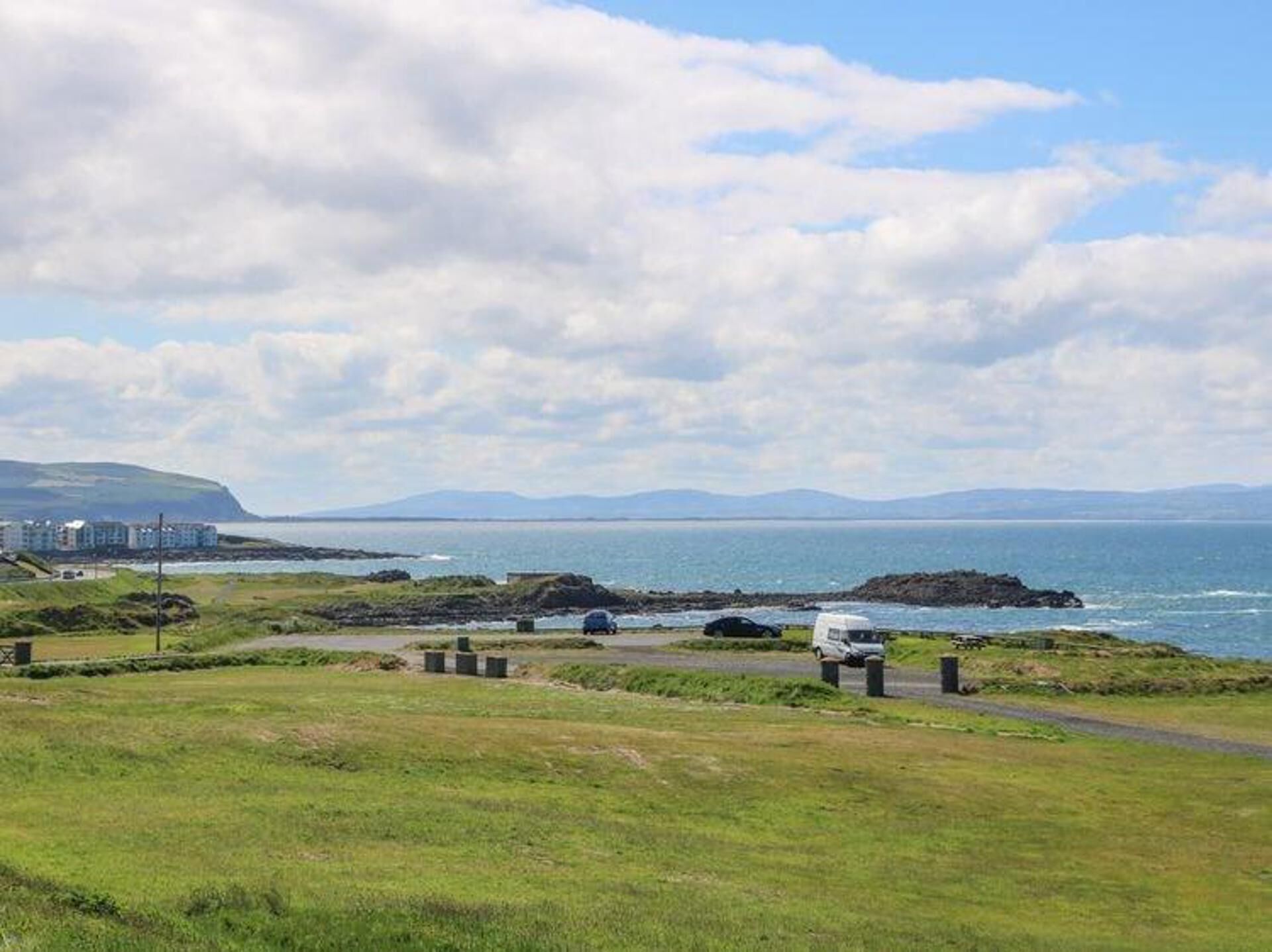 A coastal landscape with a grassy area, a road, and a body of water.