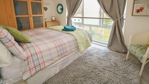 Ein Schlafzimmer mit einem Bett, einem Fenster mit Vorhängen, einem Kleiderschrank und einem kleinen Tisch.