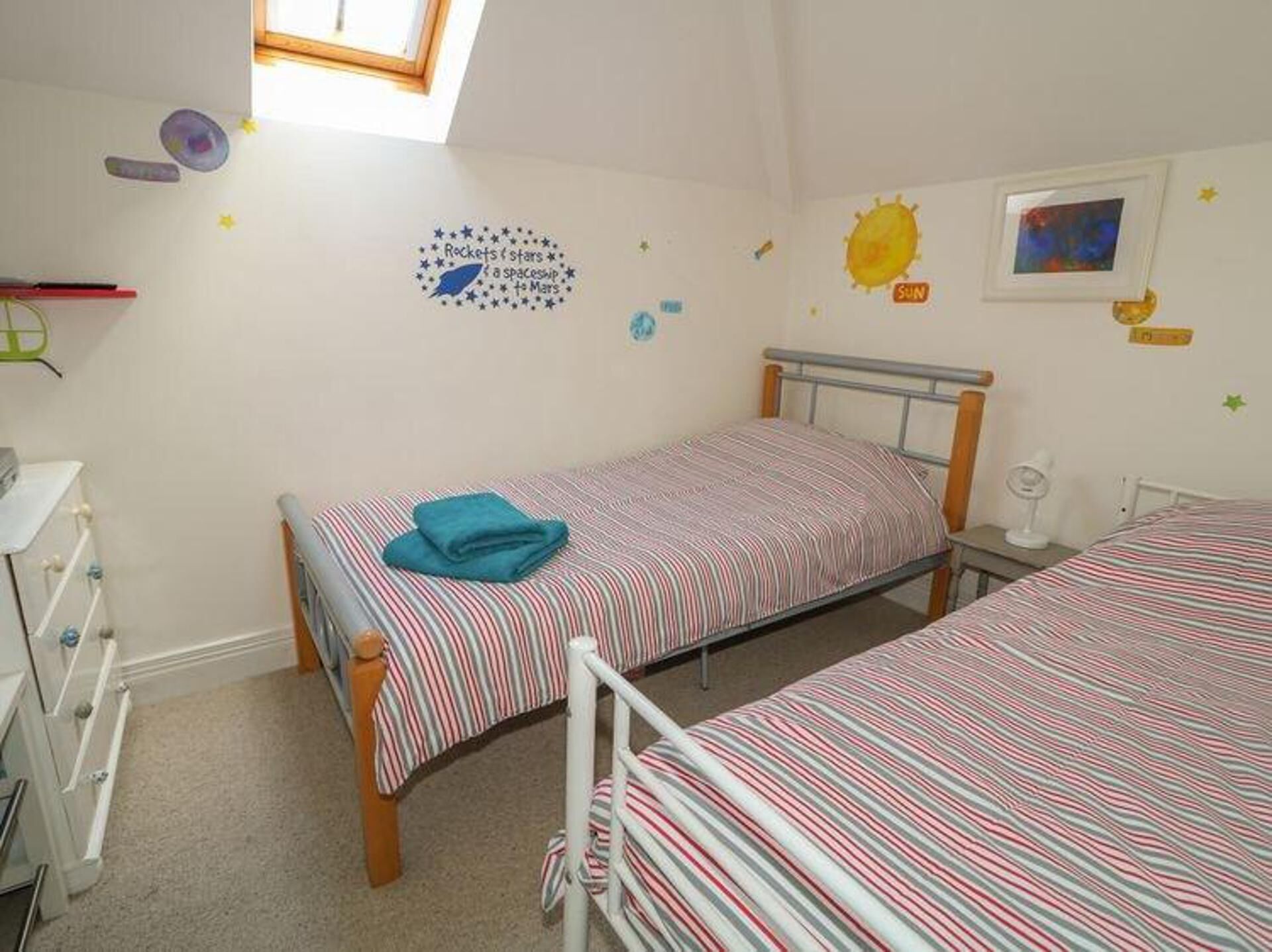A child's bedroom with two beds, a window, and wall decorations including stars and a sun.
