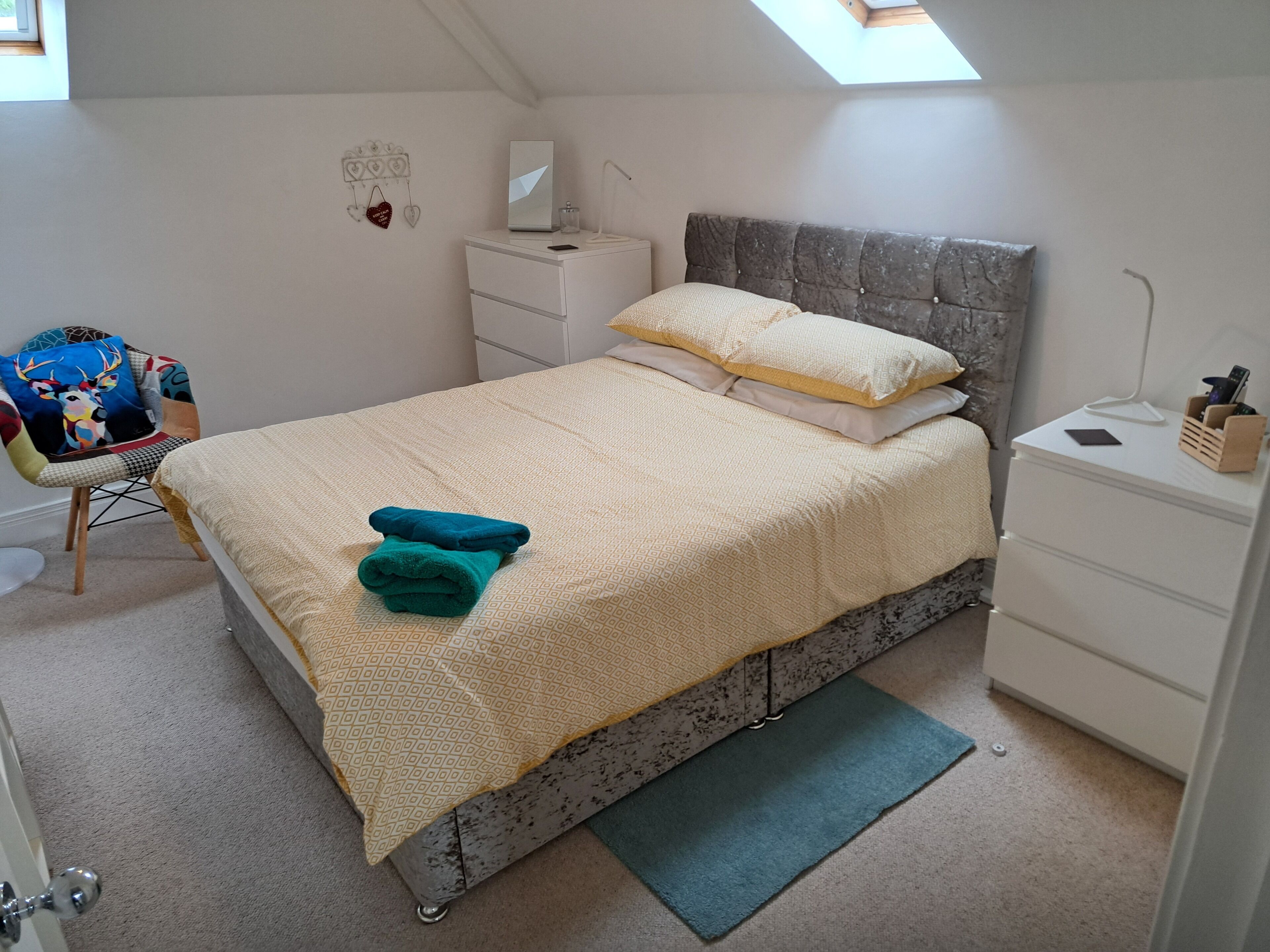 A neatly arranged bedroom with a bed, bedside tables, a chair, and a desk.