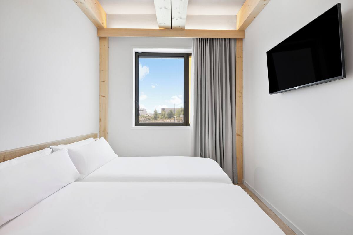 Une chambre d’hôtel moderne dotée d’un grand lit, d’un téléviseur à écran plat fixé au mur et d’une fenêtre offrant une vue sur la ville.