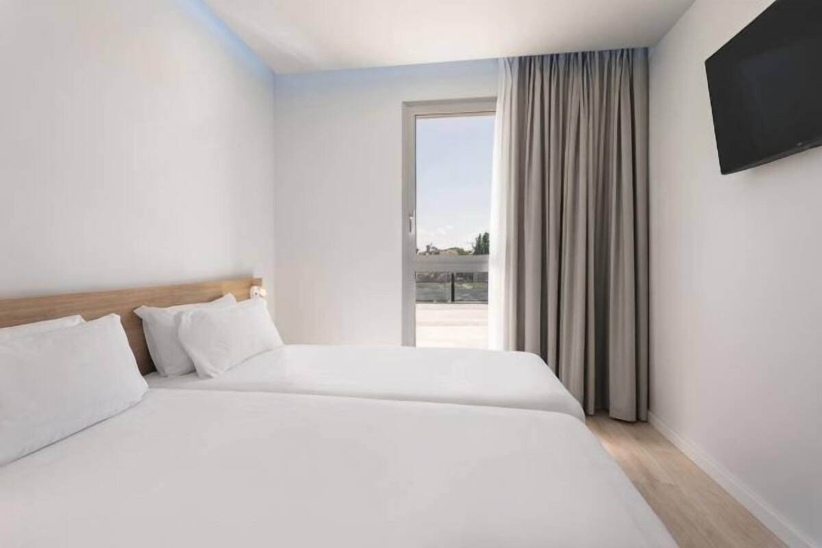 Une chambre d’hôtel avec deux lits, une télévision et un balcon avec des rideaux.