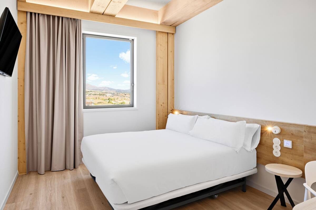 Une chambre avec un lit, une fenêtre donnant sur un beau paysage, une télévision et une petite table.