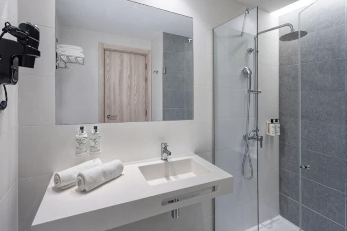 A modern bathroom with a white sink, mirror, and shower.