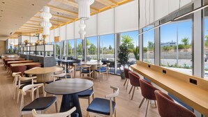 A spacious indoor area with multiple tables and chairs, large windows offering a view of the outdoors, and a modern ceiling design. - B&B Hotel Madrid Tres Cantos  (Tres Cantos)