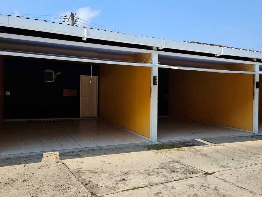 A row of unoccupied hotel rooms with a tiled floor and a metal roof.