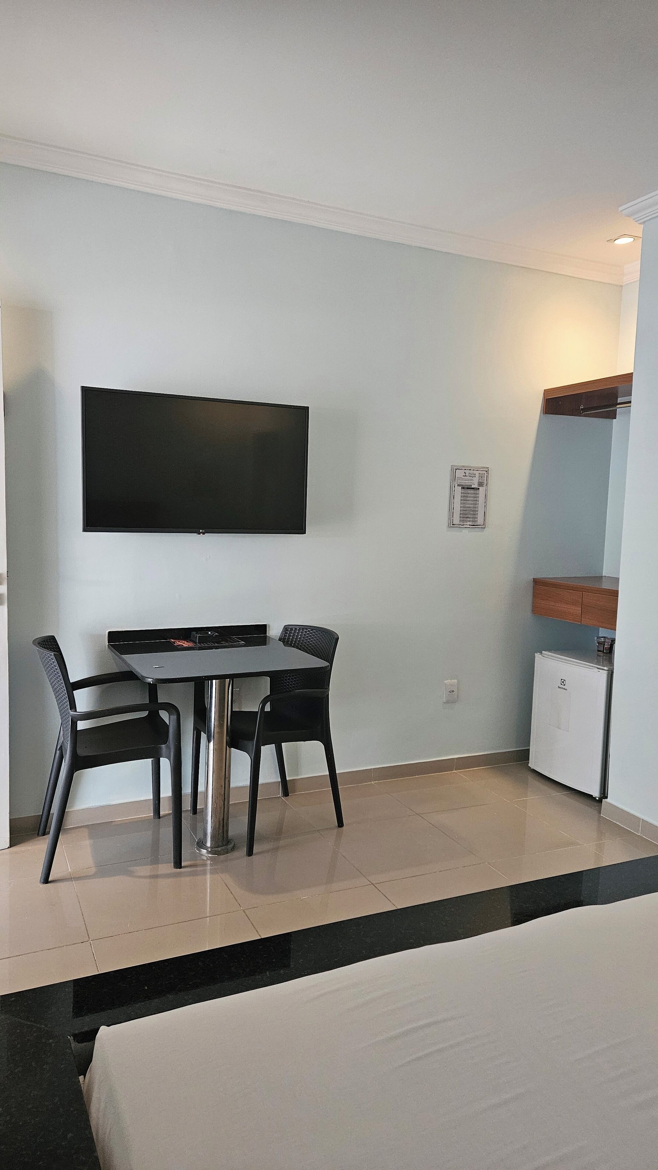 A hotel room with a bed, a TV mounted on the wall, a small table with two chairs, and a mini-fridge.