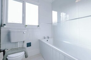 Bathroom features a white toilet, bathtub, and sink, with two windows above the sink.