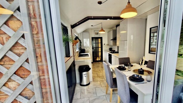 Une cuisine moderne avec des meubles blancs, un coin repas avec une table dressée pour deux personnes et une poubelle.