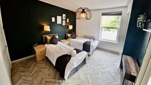 Une chambre avec deux lits, une grande fenêtre et un parquet à motifs en chevrons.